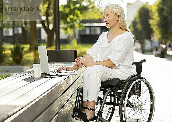 Frau im Rollstuhl mit Laptop im Freien