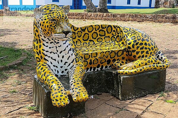 Ungewöhnliche Parkbank in Form des Aushängeschilds der Region auf dem Platz eines brasilianischen Dorfes im Schatten von Bäumen  traditionelle Häuser im Hintergrund