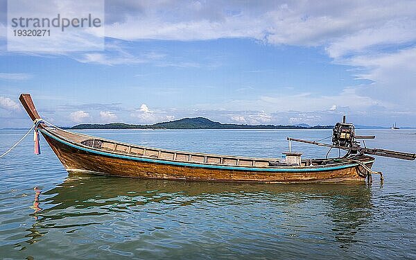 Longtailboot wartet auf Passagiere auf der schönen Insel Ko Lanta  Thailand. Die Wolken und das Boot rahmen ein Stück blaün Himmel ein Weißraum