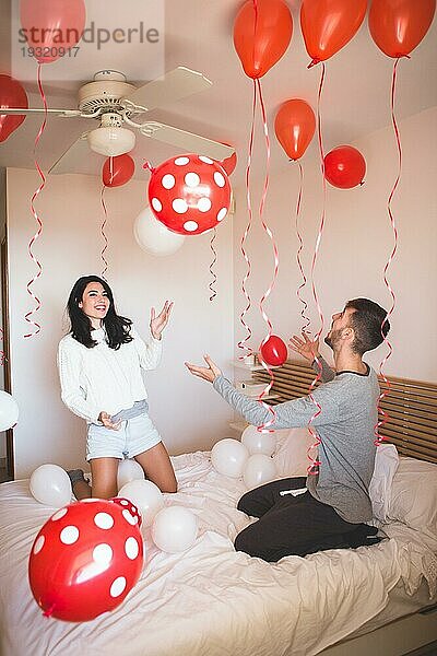 Mann lächelnd  während seine Freundin sieht Raum voller roter Ballons