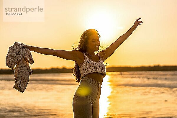 Sommerlicher Lebensstil. Eine junge blonde kaukasische Frau in einem weißen kurzen Wollpullover an einem Strand bei Sonnenuntergang. Genießen Sie den Sommernachmittag