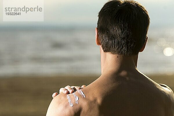 Rückenansicht Mann beim Eincremen mit Sonnenschutzmittel