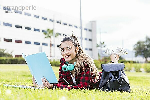 Porträt lächelnd Studentin liegend grünes Gras hält Buch Hand