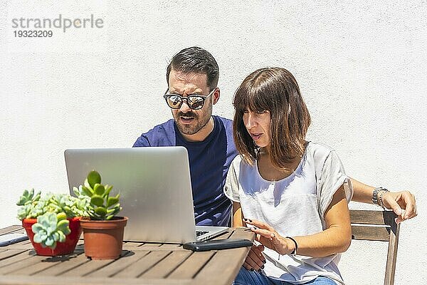 Ein Ehepaar  das zu Hause eingesperrt ist  führt einen Videogespräch mit einigen Freunden mit dem Computer  auf der Terrasse ihres Hauses mit einem weißen Hintergrund  die an einem Tisch sitzen. Viel Spaß beim Videoanruf