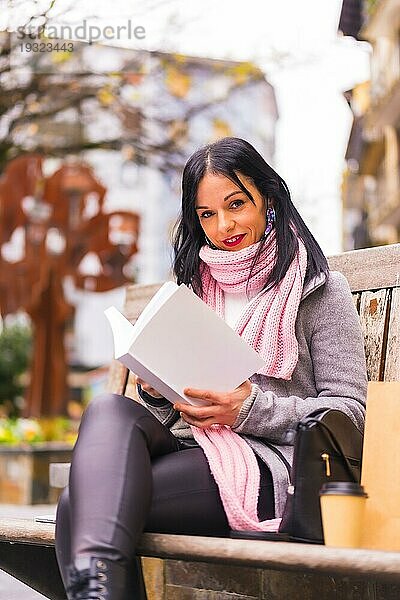 Lifestyle  kaukasisches brünettes Mädchen liest ein Buch in einem Park  lächelnd auf einer Bank sitzend