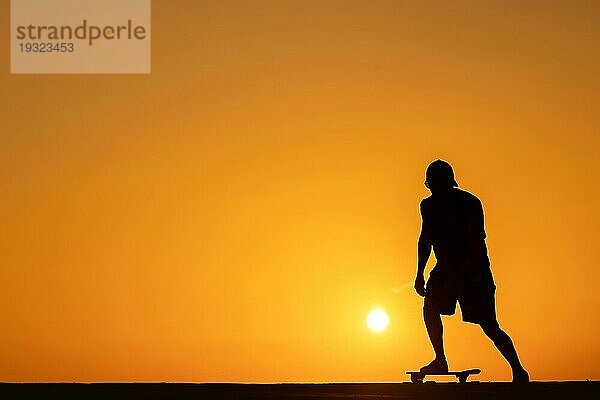 Silhouette eines Mannes auf einem Skateboard bei leuchtend orangefarbenem Sonnenuntergang. Mittlere Aufnahme