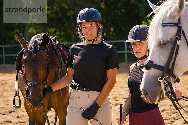 Zwei junge kaukasische Reiterinnen haben Spaß mit ihren weißen und braunen Pferden beim Reiten  schwarz gekleidet mit Schutzkappen