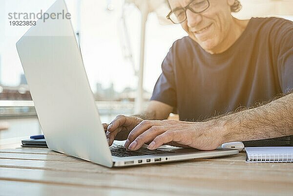 Lächelnder älterer Mann  der einen Laptop im Café benutzt