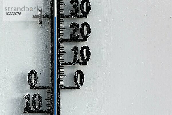 Klassisches schwarzes analoges Thermometer  das an einer weißen Wand hängt und eine blaue Temperaturskala von dreißig  30 Grad Celsius anzeigt