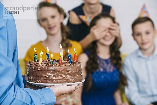 Close up Junge s Hand bringt Schokolade Kuchen Geburtstagskind mit bedeckten Augen von ihrem Freund