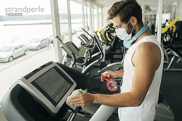 Seitenansicht Mann mit medizinischer Maske beim Desinfizieren des Laufbands im Fitnessstudio