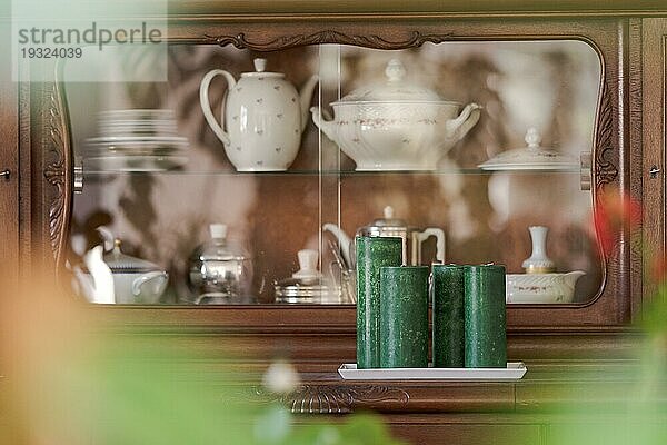 Vorderseite einer alten hölzernen Anrichte  gefüllt mit Großmutters Teekannen und Tellern  gesehen durch den verschwommenen Vordergrund der Zimmerpflanzen