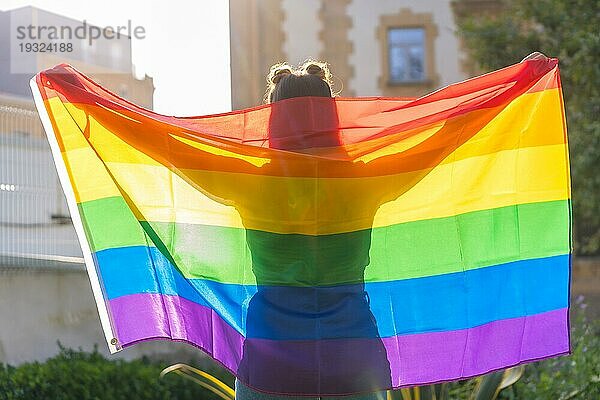 Eine Nahaufnahme von einer jungen kaukasischen weiblichen Silhouette hinter LGBT Stolz Flagge im Freien