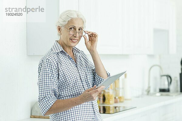 Porträt lächelnd ältere Frau hält digitale Tablette stehend Küche