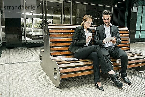 Geschäftsleute  die auf einer Bank sitzen und auf ein Mobiltelefon schauen