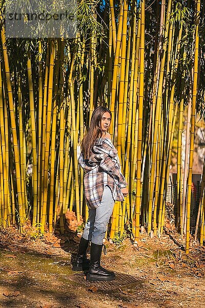 Herbstlicher Lebensstil  junges kaukasisches brünettes Mädchen in einem karierten Wollpullover und zerrissenen Jeans in einem Bambushain