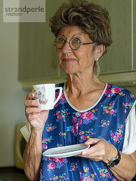 Oma mit alter Kittelschürze  Brille und Perücke in der Küche  hält Kaffeetasse in Händen  Deutschland  Europa