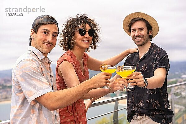 Frau und Männer  die sich im Urlaub amüsieren und Cocktails auf einer Terrasse mit Meerblick trinken