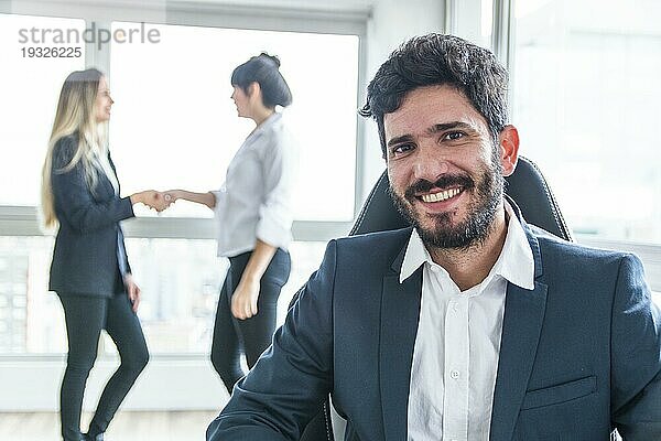Porträt lächelnder Geschäftsmann vor Frauen beim Händeschütteln