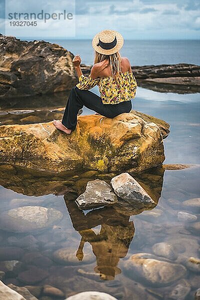 Mädchen in geblümter Bluse  schwarzen Shorts und Strohhut in einer Naturlandschaft am Meer