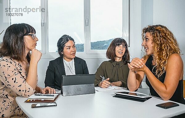 Sitzung junger Unternehmer im Büro  junger Mann lateinamerikanischer Abstammung und drei junge kaukasische Frauen bei einem Tischgespräch