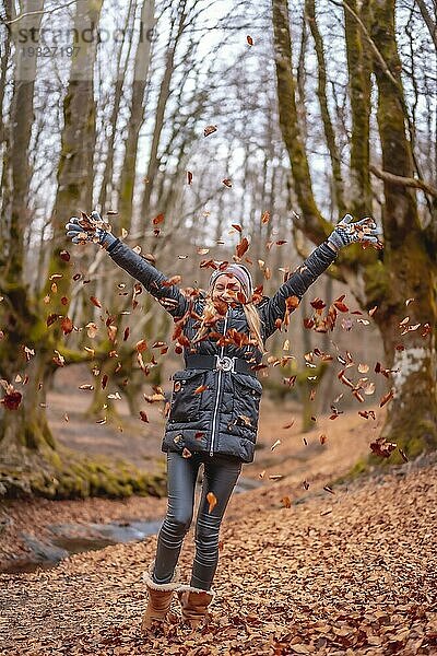 Sehr glückliches blondes Mädchen spielt mit Blättern in einem schönen Wald