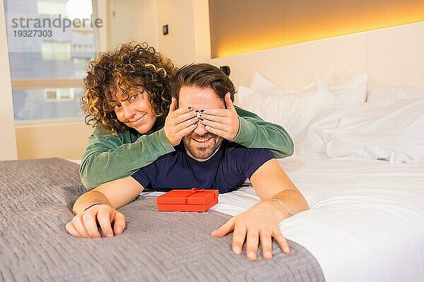 Valentinstag  ein junges kaukasisches Paar im Schlafanzug auf dem Bett  die Braut überrascht ihren Freund mit einem netten Geschenk