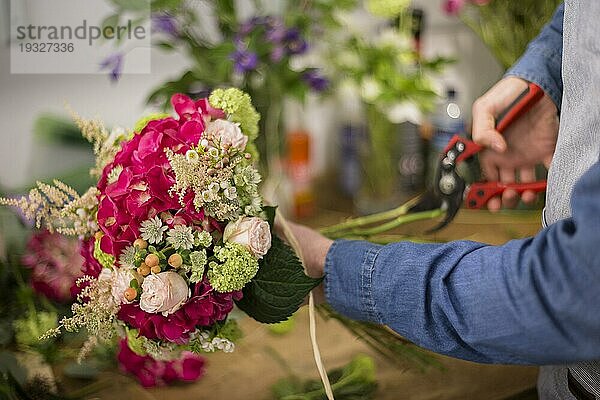 Männlicher Florist schneidet bunte Blumenstraußzweige mit einer Gartenschere