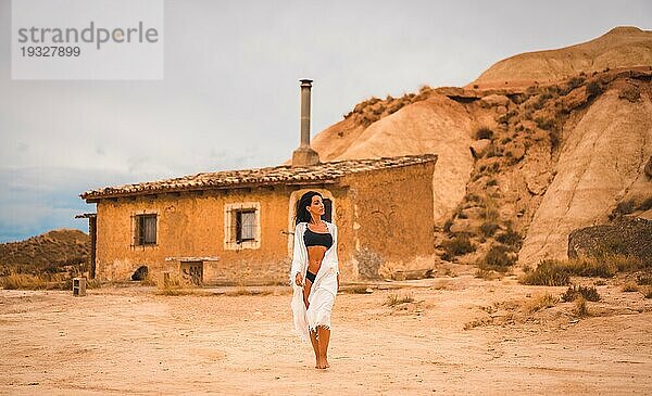 Eine junge brünette Kaukasierin in einem weißen Kleid und einem schwarzen Bikini posierte in der Wüste von Las Bardenas  Navarra. Spanien