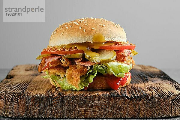 Kentucky Chicken Burger mit eingelegter Gurke und frischer Tomate auf Holzuntergrund  Vorderansicht