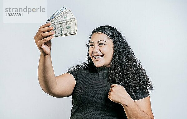 Aufgeregtes lateinamerikanisches Mädchen  das einen Dollar in bar hält  isoliert. Siegreiche junge Frau hält Geld feiern isoliert