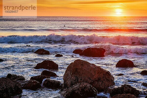 Sonnenuntergang über dem Atlantik mit Wellen und Felsen und Surfer Silhouetten im Wasser an der Costa da Caparica  Portugal  Europa