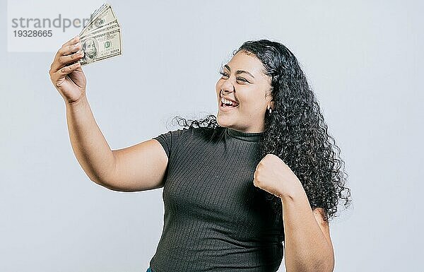 Siegreiche junge Frau hält Geld feiernd isoliert. Aufgeregtes lateinisches Mädchen hält Dollar Bargeld isoliert
