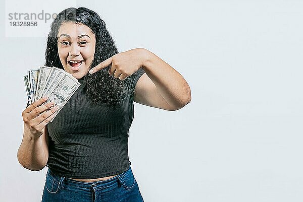 Lächelnde junge Frau  die Geld hält und darauf zeigt  isoliert. Attraktives lateinisches Mädchen  das Geld hält und darauf zeigt. Lateinische Menschen halten Geld
