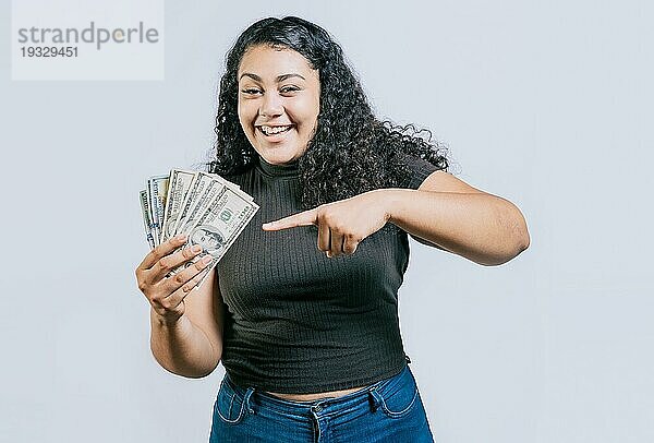 Attraktives lateinisches Mädchen  das Geld hält und darauf zeigt. Lächelnde junge Frau  die Geld hält und darauf zeigt  isoliert. Lateinische Menschen halten Geld