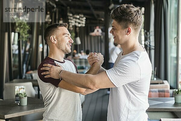Zwei glückliche junge männliche Freunde schütteln Hände Restaurant