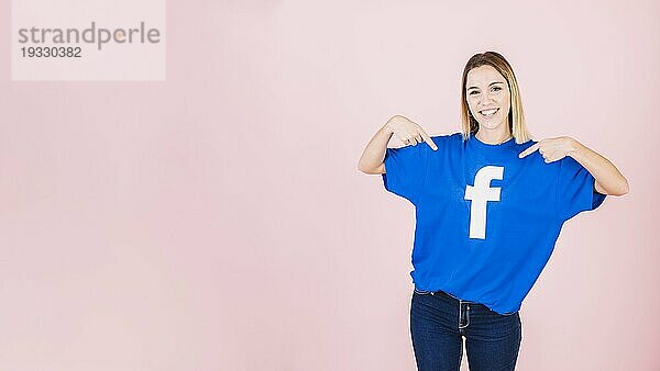 Porträt glückliche junge Frau  die ihr TShirt mit Facebooksymbol zeigt