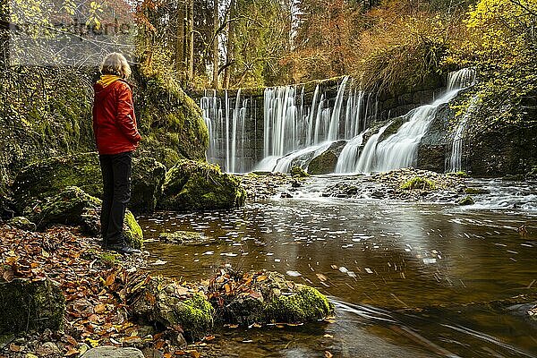 Der Geratser Wasserfall im Herbst. Eine Wanderin steht am Ufer. Moosbedeckte Felsen an den Seiten  Bäume im Herbstlaub. Gerats  Oberallgäu  Allgäu  Bayern  Deutschland  Europa