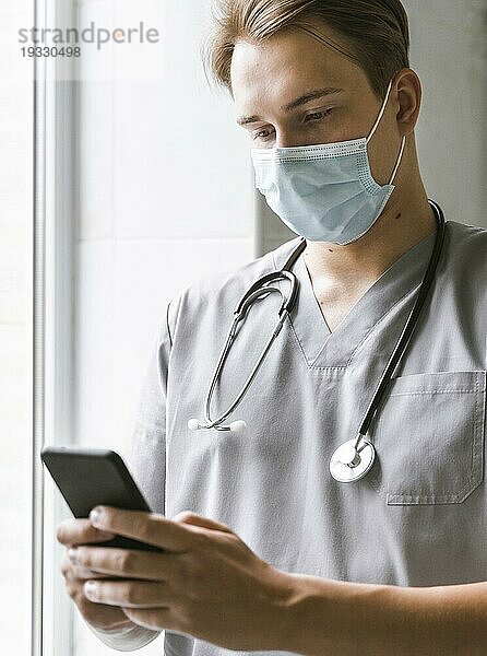 Arzt mit medizinischer Maske prüft Smartphone