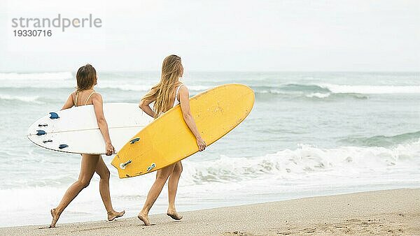 Zwei lächelnde Freunde laufen am Strand mit Surfbrettern