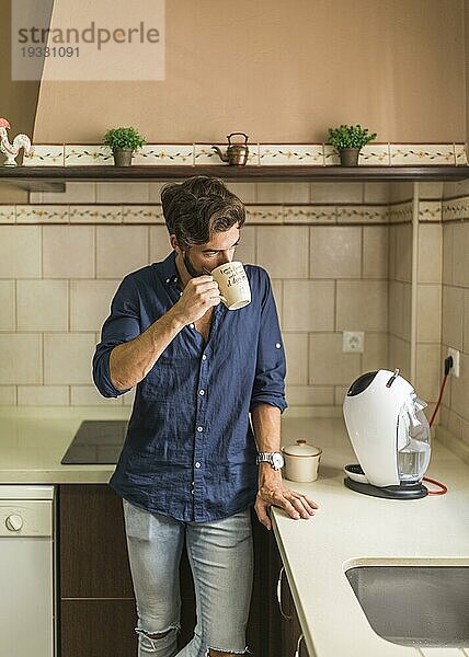 Mann steht in der Küche und trinkt Kaffee