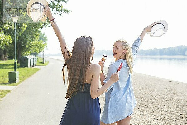Zwei junge Freundinnen mit Hut genießen Eis am Strand
