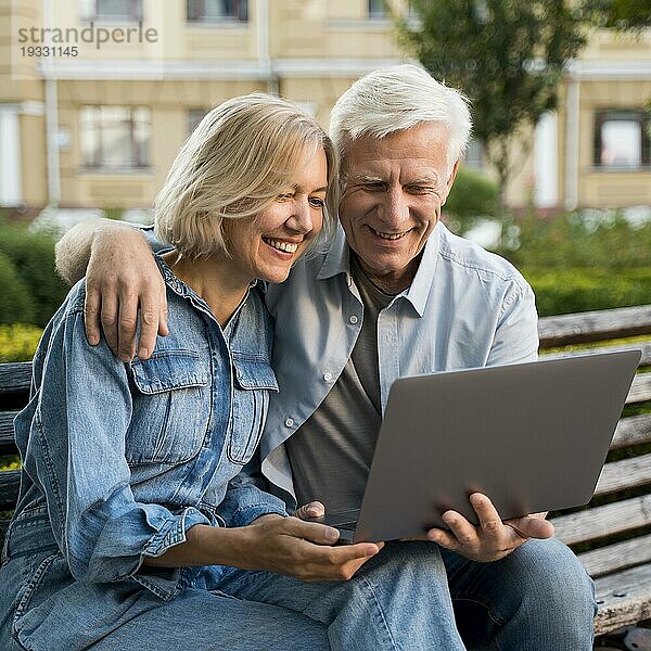 Lächelndes älteres Paar auf einer Bank im Freien mit Laptop