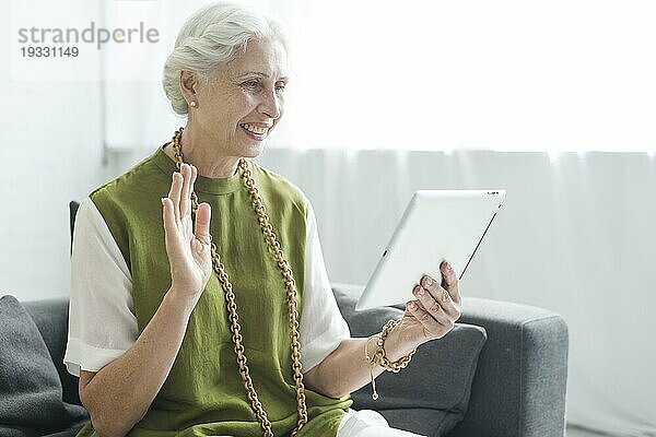 Glückliche Frau  die auf dem Sofa sitzt und sich von ihrem digitalen Tablet verabschiedet