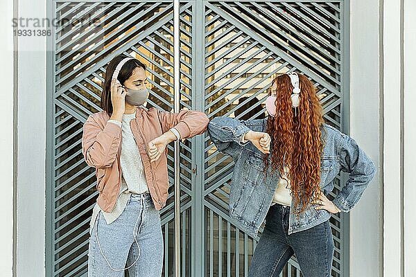 Frontansicht Freundinnen mit Gesichtsmasken im Freien beim Ellbogengruß