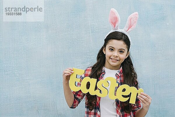 Lächelnde Porträt Mädchen hält gelbe Ostern Wort suchen Kamera