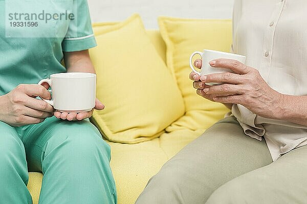 Close up Krankenschwester Patienten sitzen Sofa halten Kaffeetassen