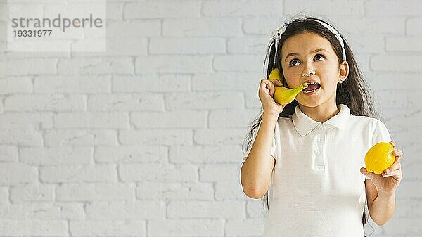 Verrücktes Mädchen hält Zitrone ihre Hand macht Spaß mit gelben Banane