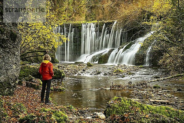 Der Geratser Wasserfall im Herbst. Eine Wanderin steht am Ufer. Moosbedeckte Felsen und Bäume im Herbstlaub. Gerats  Oberallgäu  Allgäu  Bayern  Deutschland  Europa