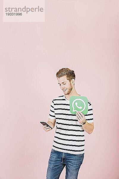 Glücklicher junger Mann mit Whatsapp Symbol und Smartphone